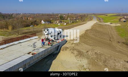 Above view, overhead on construction workers are spreading and leveling fresh concrete in square trench after pouring from mixer truck on unfinished b Stock Photo