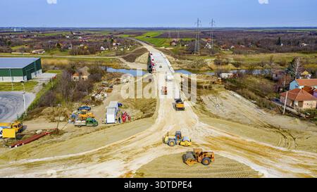 Above view, on circular road, roundabout under construction, crew of workers at building site working on road foundation with heavy machinery Stock Photo