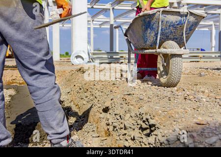 Construction worker is using shovel to unloading cement from wheelbarrow on construction site Stock Photo