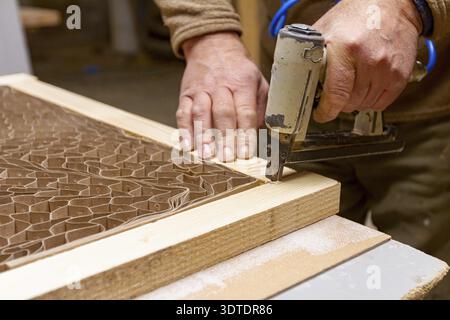 Carpenter puts together planks on the door frame using a pneumatic stapler in the carpentry workshop Stock Photo