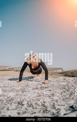 Woman Doing Push-Ups on a Rocky Cliff with a Blue Sky Stock Photo