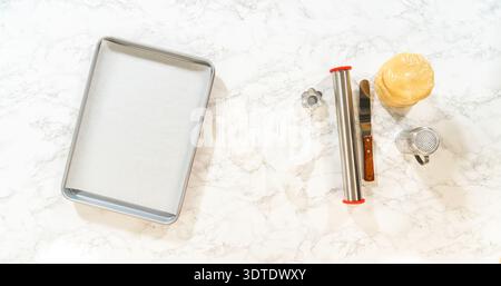 A top view of baking tools including dough disks, cookie cutter, rolling pin, gloves, and a baking tray, laid out for Easter Cookie Sandwich preparati Stock Photo