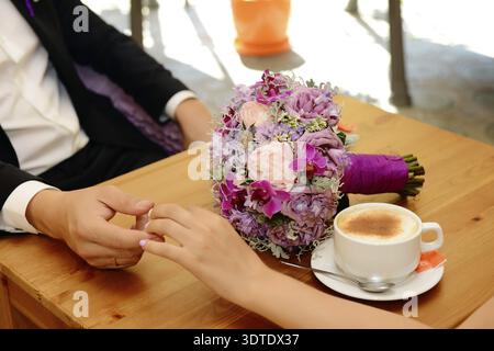 Bride and groom holding each other's hands while sitting at the table Stock Photo