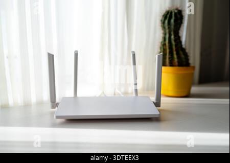 Modern wireless router on a white table in a bright minimalist interior. High-speed home internet connection, technology, and remote work concept in a Stock Photo
