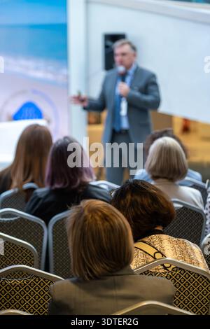 Professional speaker presents at conference addressing attentive audience in corporate setting. Stock Photo