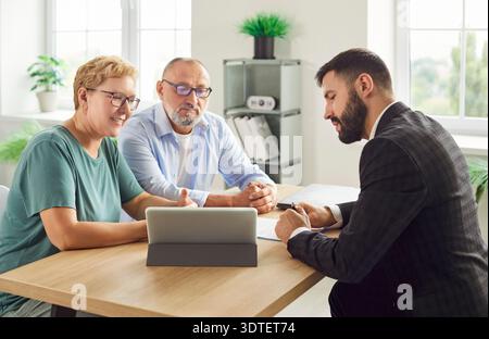 Couple signing documents with financial advisor at office desk using tablet Stock Photo