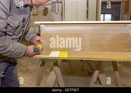 Worker in carpentry uses professional manual power tool, acu drill, and twists the screws on the wooden door frame Stock Photo