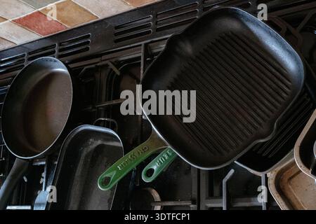 Black gas stovetop cluttered with several cast iron cooking pans in a warm-toned kitchen setting. Concept food, cooking, cast-iron utensils. Stock Photo