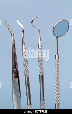 Macro studio shot of stainless dental instruments including tweezers, dental mirror, scaler, and explorer arranged on a clean blue background. Profess Stock Photo