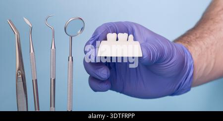 Dentist Hand in Blue Medical Glove Holding Dental Crown Shade or Prosthetic Tooth Model with Dental Instruments Stock Photo