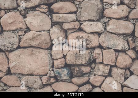 The image presents a close-up view of a stone wall, showcasing its texture and structure. The wall is composed of variously sized and shaped stones, p Stock Photo