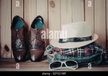 A pair of brown leather shoes, a white hat, folded plaid shirt and sunglasses on a wooden background Stock Photo