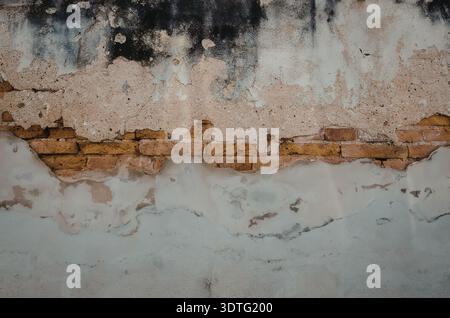 a close-up of a damaged brick wall with peeling paint and exposed bricks Stock Photo