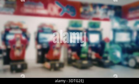 A blurry image of several arcade machines in a row, with colorful designs and screens, set against a white wall with a red banner. Stock Photo