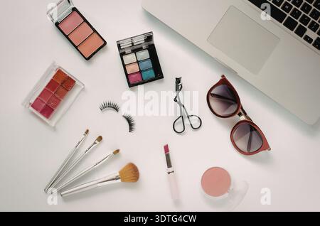 The image features a collection of beauty products and a laptop on a white surface. The products include a makeup palette, lip gloss, eyelashes, sciss Stock Photo