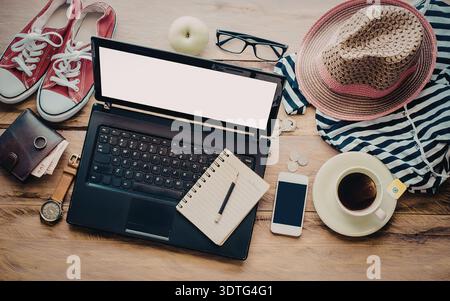 A laptop, shoes, hat, coffee, and other accessories on a wooden table Stock Photo