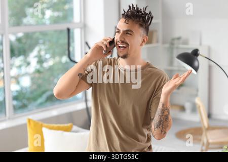 Young man with dreadlocks talking by mobile phone at home Stock Photo