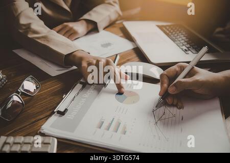 Two people sitting at a desk analyzing data on papers with a laptop and glasses nearby. Stock Photo