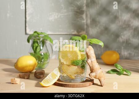 Glass of infused water with basil leaves, ginger and lemons on light wooden table against grey grunge wall Stock Photo