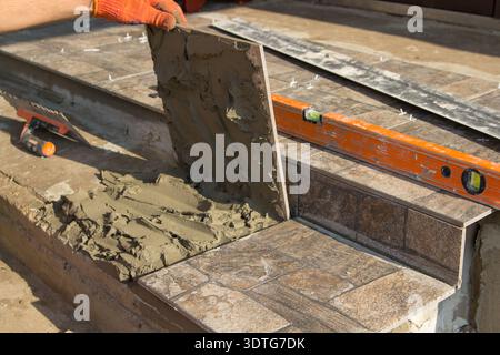 The builder works on stairs puts a tile of stone on the stairs to the office Stock Photo