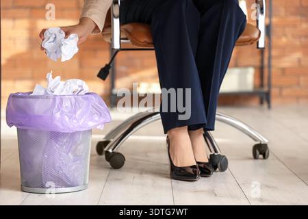 Businesswoman throwing crumpled paper into trash bin in office, closeup Stock Photo