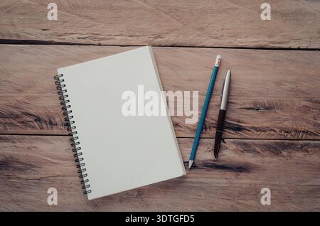 A spiral-bound notebook lies open on a wooden desk alongside two paintbrushes. Stock Photo