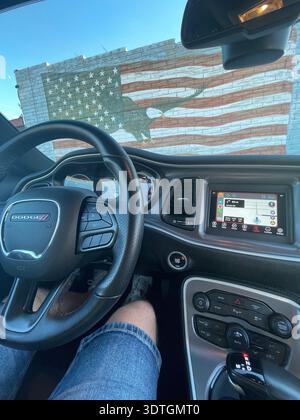 View from inside a Dodge car with steering wheel and dashboard, parked in front of a wall mural of the American flag with eagle silhouette, USA. Stock Photo