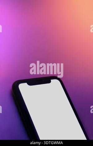 Close up of smartphone with white screen on pink purple neon surface. Copy space for app, product, or user interface presentation. Vertical banner of phone mock up with blank screen Stock Photo