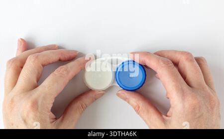 Woman's hands holding a contact lens case on white background. Empty white plastic lens case with compartments for storing contact lenses. Concept for Stock Photo
