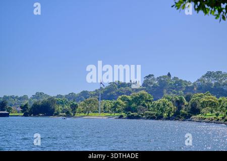 A tranquil waterside landscape bathed in bright sunlight, featuring a calm blue body of water reflecting the clear sky. Stock Photo