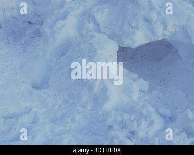 A snow covered hill with a small hole in the middle. The snow is white and the hole is black Stock Photo