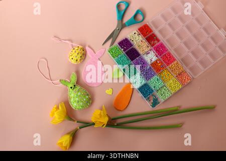 Easter decoration with eggs, hand made bunny, colorful seed beads and daffodils on pink background Stock Photo