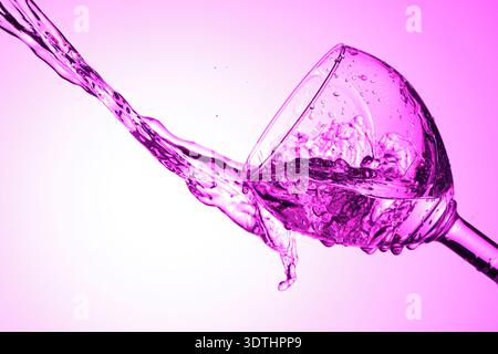 Liquid splashes from tilted glass with purple lighting. Stock Photo