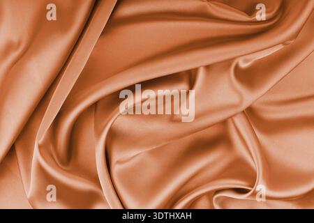 Crumpled, wrinkled orange colored glossy silk satin with wave drapery.. Shiny smooth fabric with soft folds, cloth texture . Elegant rich background, Stock Photo