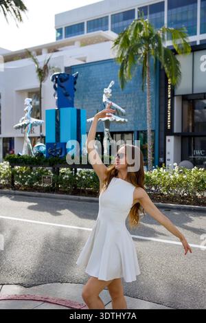 Woman dancing in white dress near ballerina sculptures Beverly Hills California Stock Photo