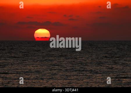 The sun in an orange sky setting behind the sea waves. Stock Photo