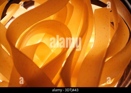 Warm close-up of curled wide pasta strips illuminated from behind, creating abstract ribbon-like shapes and soft golden tones. Stock Photo