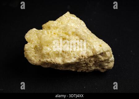 Pale yellow crystalline rock on black background, rough porous texture, triangular shape Stock Photo