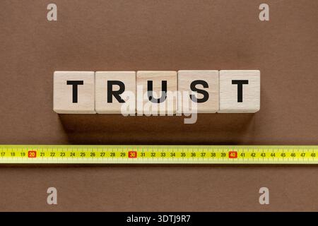Measure of trust. Business and financial concept. The word TRUST on a wooden block and a measuring tape. Build trust in business. Brown. Close upbackg Stock Photo
