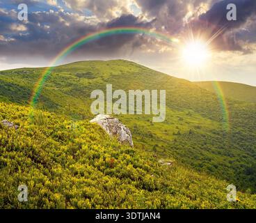 mountain landscape during summer at sunset. alpine meadows on green slopes and hills in evening light. amazing adventure scenery under rainbow. explor Stock Photo