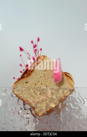 Abstract still life composition featuring a slice of bread with pink floral accents, partially obscured by textured glass. Dreamy surreal concept blen Stock Photo