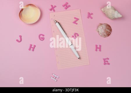 Sea shells and random pink letters, a pen and paper on pink surface. Stock Photo