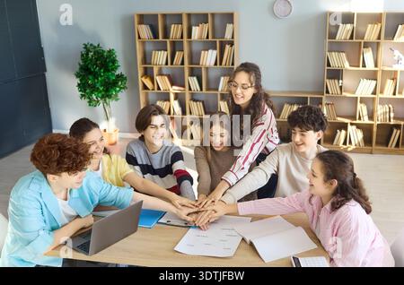 Happy teen students stacking hands during teamwork in library study group Stock Photo