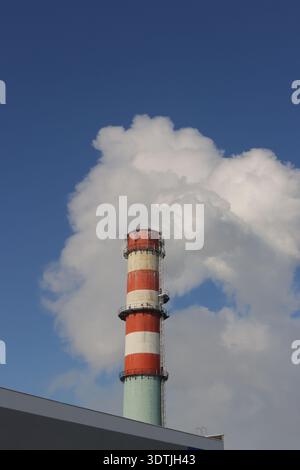 A tall red and white tower with smoke coming out of it. Thick white smoke billows out of a large factory chimney. Stock Photo