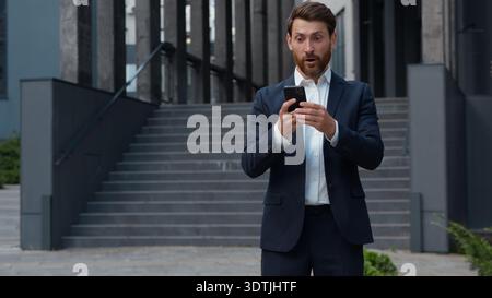 Happy excited Caucasian mature business man successful win with phone in city yelling happy winner middle-aged businessman male entrepreneur winning Stock Photo