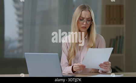 Caucasian business woman with laptop working confused checking paper documents mistake female girl businesswoman manager worker difficult job online Stock Photo