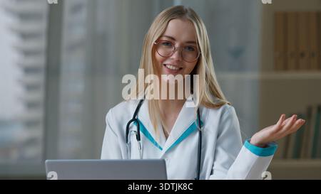 Happy smiling doctor Caucasian woman girl female nurse talking looking at camera lady in uniform consulting patient laptop talk communicating in Stock Photo