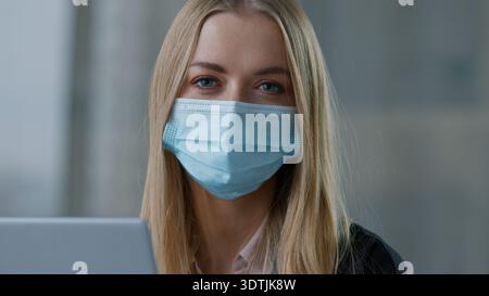 Portrait Caucasian business woman in face medical protective mask in office with laptop working businesswoman ill girl sick female entrepreneur Stock Photo