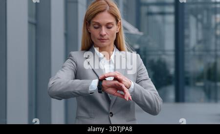 Serious Caucasian middle-aged business woman checking time with wristwatch in city looking around waiting meeting adult businesswoman female worker Stock Photo