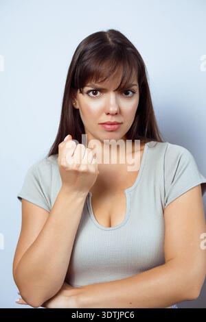 Serious young woman clenching fist with determined expression isolated on neutral studio background. Stock Photo